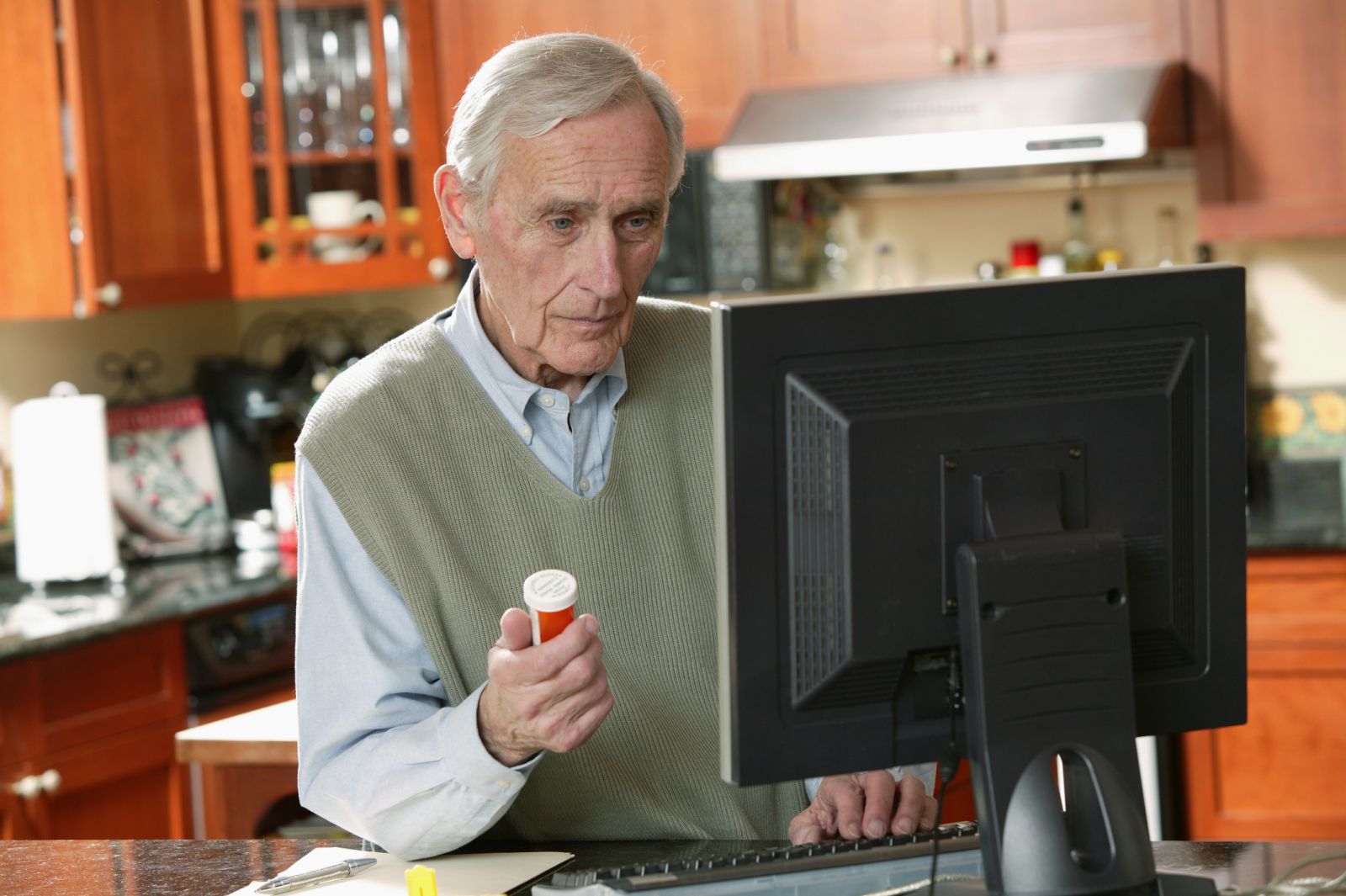 Bilde av en eldre person som sitter foran en PC med pilleeske i hånda